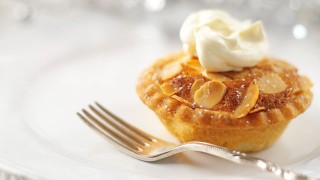 Mini Mincemeat Bakewell Tarts served on a white plate, with a silver fork and served with a dollop of cream