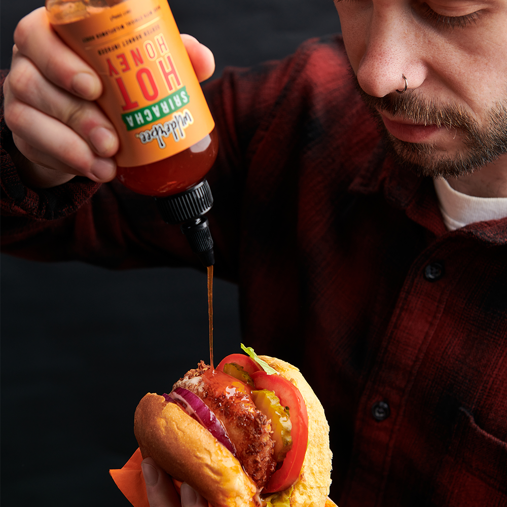 Hot honey being poured on to a chicken burger