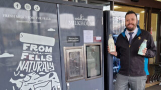 Matt Welsh Store Manager with the Midtown Milkhouse vending machine. Matt is holding two glass bottles of milk.