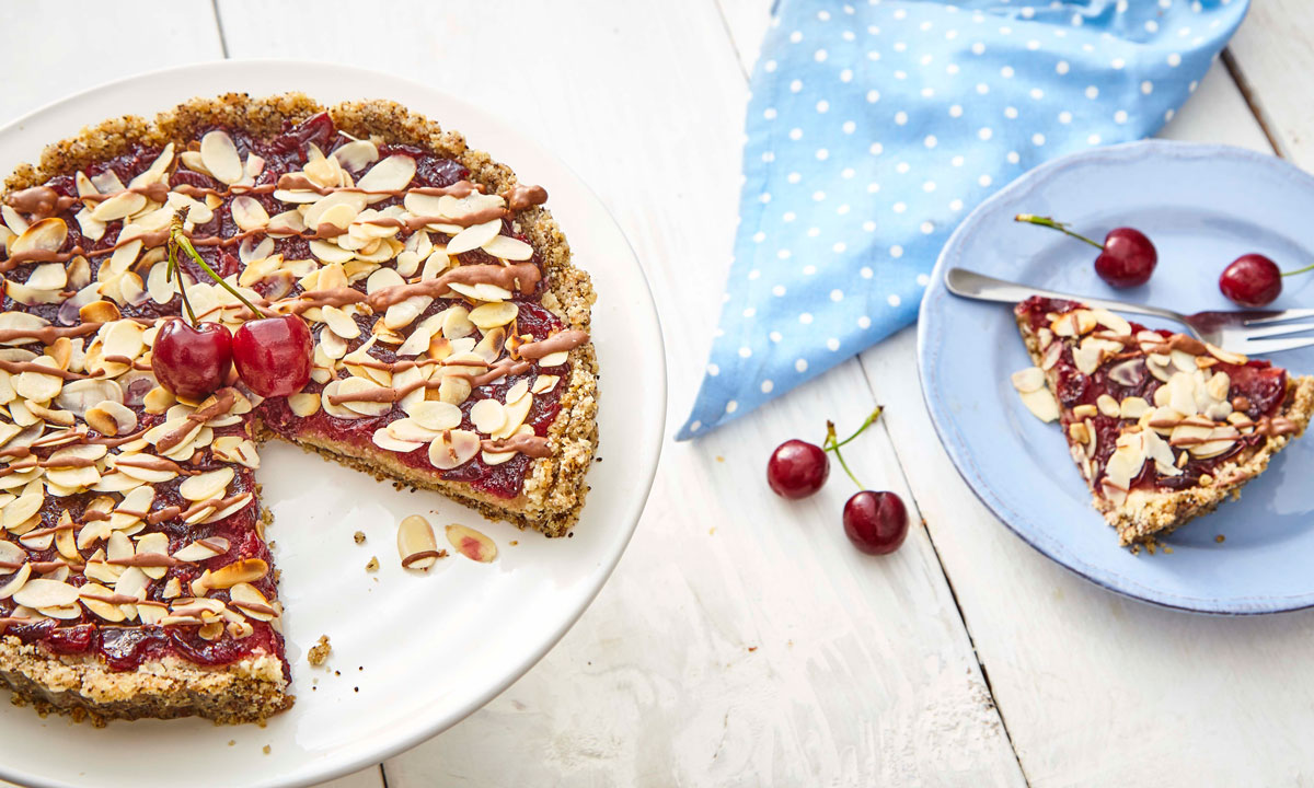 No Bake Cherry Bakewell served on a white dish, with a sliced removed and to the side on a blue plate