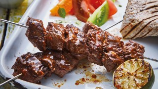 Brazilian Churrasco Beef Kebabs served on a white plate with coloured tomato salad