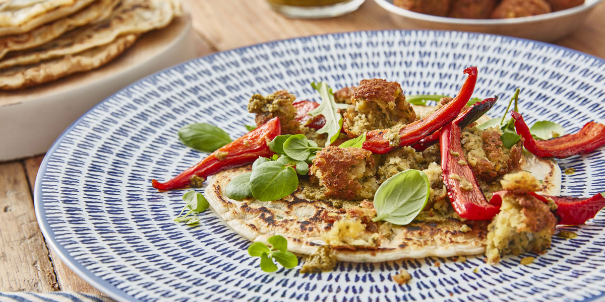 Spelt Pancakes with Falafels on a blue and white plate, topped with roasted red peppers and basil