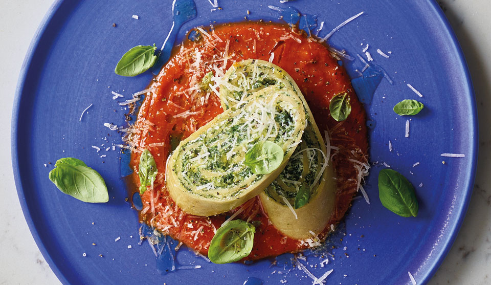 Spinach and Rocitta Pasta Roll sliced and oin top of the tomato sauce on a blue plate