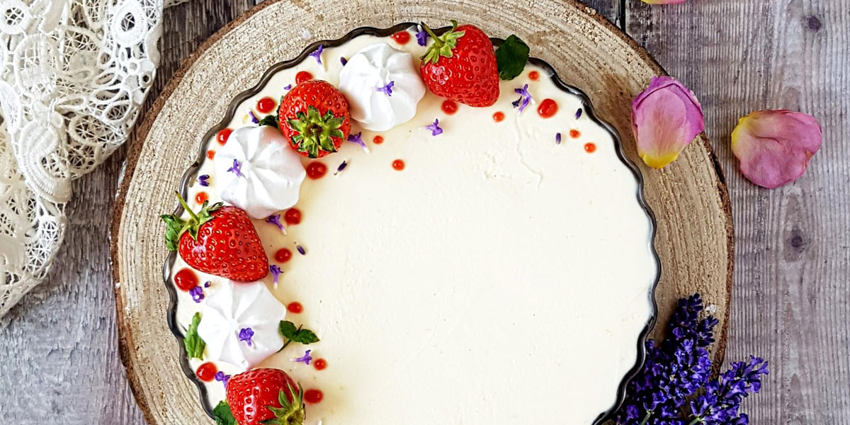 Cream Tea Cheesecake served on a wooden board, topped with strawberries and mini meringues