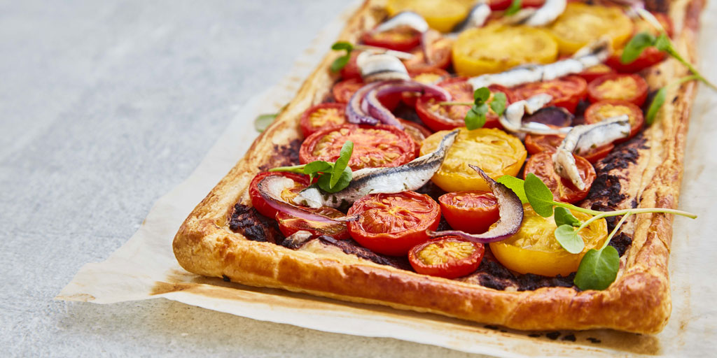 Tomato, Tapenade and Anchovy Tart served on baking parchment and topped with watercress